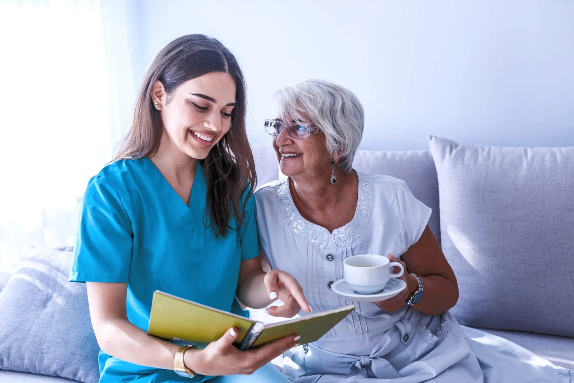 A Harmony carer sitting with an elderly client, sharing a book and a cup of tea at home in Suffolk